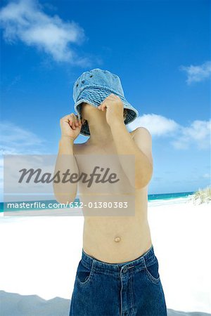 Boy pulling hat down over face on beach