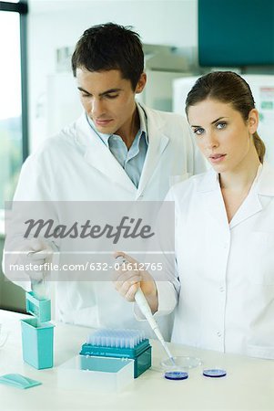 Male and female lab workers standing side by side, woman looking at camera