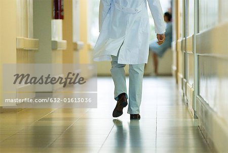 Male doctor walking in hospital corridor, cropped rear view