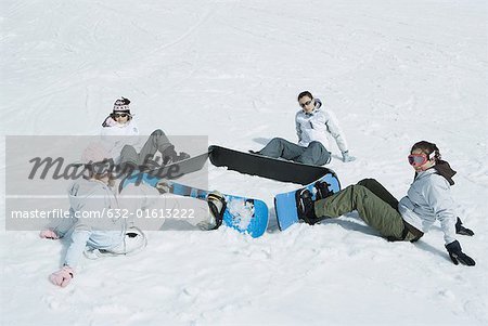 Four young snowboarders sitting on the ground in a square, looking at camera