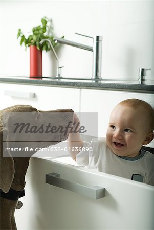 Baby in drawer smiling as dog sniffs baby's hand
