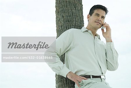 Man leaning against tree trunk, using cell phone, waist up