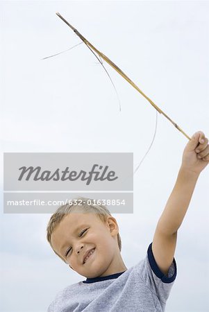 Boy holding up stick, smiling, squinting eyes closed, low angle view