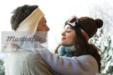 Young couple in winter clothing, woman with arms around man's neck, side view