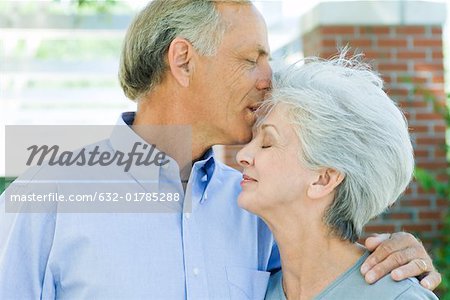 Mature man kissing wife's forehead, side view