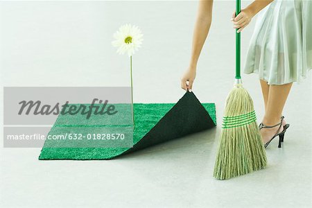Woman sweeping under artificial turf rug, waist down
