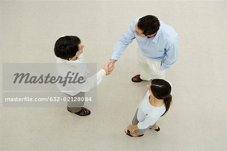 Two men shaking hands, female colleague watching, overhead view
