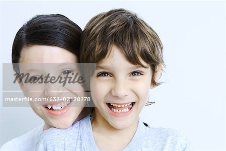 Sister behind her brother head resting on his shoulder, smiling at camera, portrait