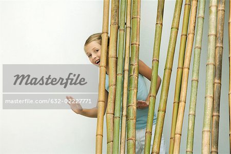 Girl standing behind bamboo, smiling and waving at camera