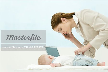 Professional woman in office, using cell phone, bending over baby on desk