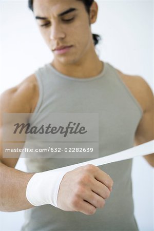 Man wrapping bandage around his wrist, looking down