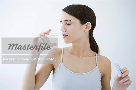 Woman drinking effervescent water, holding medicine packet