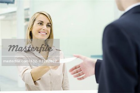 Woman smiling, handing document to businessman