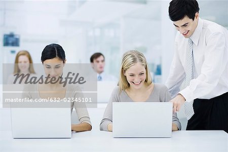 Female office worker using laptop computer, male supervisor looking over her shoulder and pointing