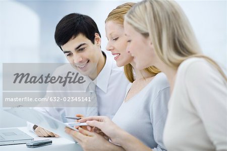 Three colleagues reading document on clipboard, smiling