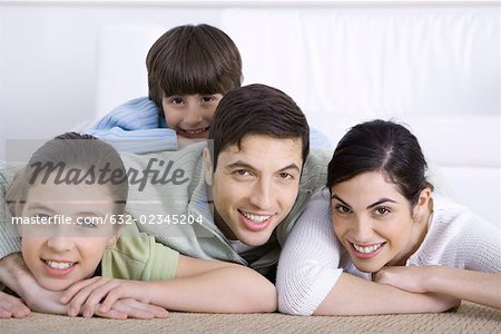 Portrait of smiling family lying together on floor, son lying on his father's back