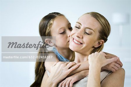 Mother and daughter embracing, girl kissing woman's cheek