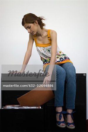 Woman sitting on top of filing cabinets, reviewing contents of file