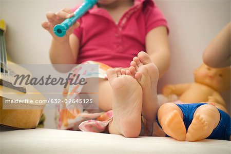 Little girl sitting with legs crossed, playing recorder, cropped