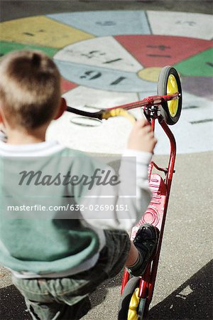 Boy playing with scooter on playground, rear view