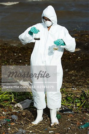 Person in protective suit holding up flasks filled with polluted water