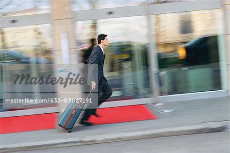 Businessman running down sidewalk, pulling suitcase behind him