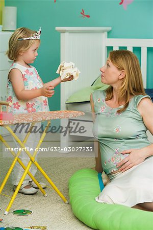 Pregnant mother playing with little girl in nursery