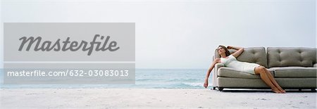 Woman reclining on couch on beach at water's edge