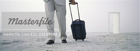 Man walking with rolling luggage on beach, open door in distance