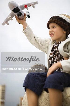 Little boy sitting on father's shoulders, holding up toy airplane