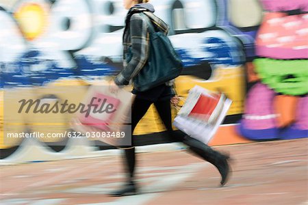 Pedestrian carrying shopping bags on sidewalk, blurred