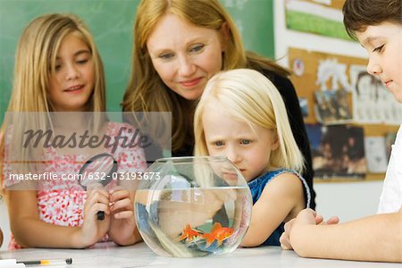 Elementary teacher and students gathered around goldfish bowl