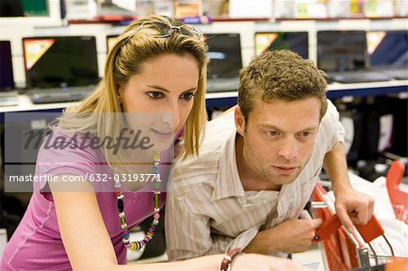 Couple together in electronics section of department store, shelf of laptops in background