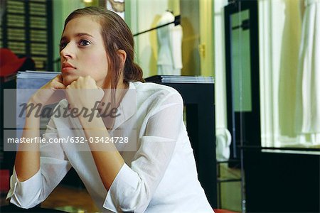 Young woman sitting with hands under chin, looking away in thought