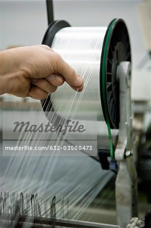 Weaving mill, machinist manually checking thread tension