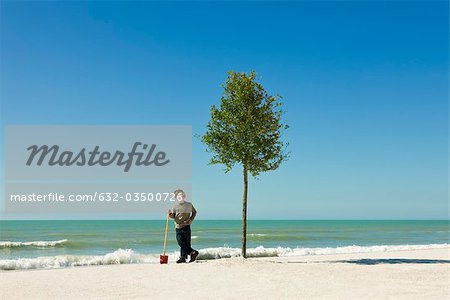 Boy standing with shovel beside tree planted on beach