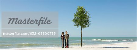 Children standing with shovels beside tree planted on beach