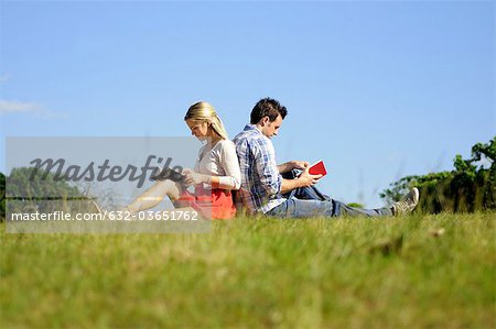 Couple sitting back to back reading in park