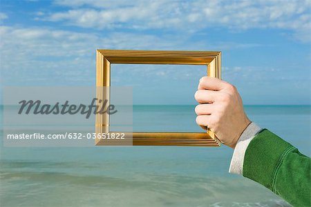 Person holding picture frame in front of ocean