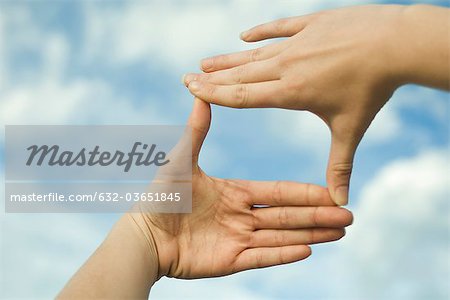Hands making a finger frame in front of sky