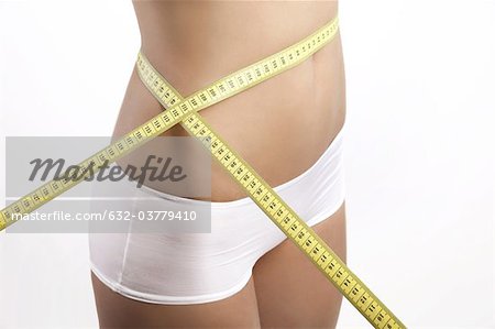 Young woman measuring waist with measuring tape, cropped