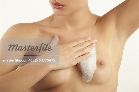 Young woman applying moisturizer to bare chest, cropped