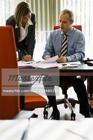 Businessman talking to female colleague as she making notes
