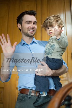 Father and toddler son waving at camera