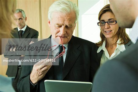 Mature executive examining information on digital tablet with colleagues