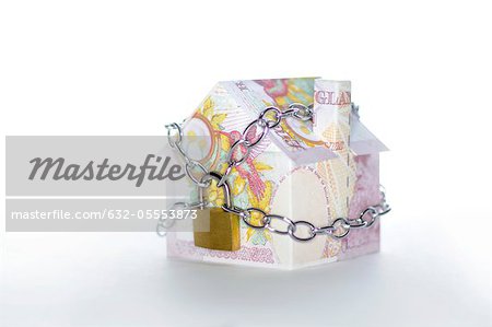 Model house folded with British pound banknotes chained and padlocked