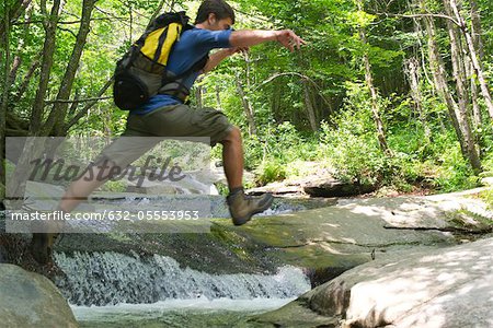 Man jumping over stream through woods
