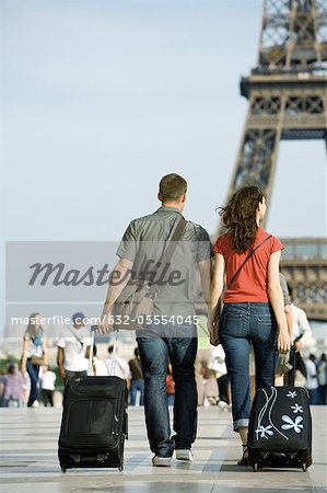 Couple walking with rolling luggage near Eiffel Tower, Paris, France