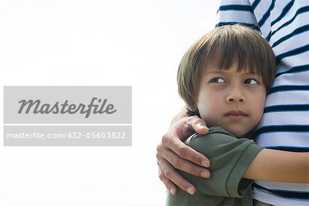 Boy embracing his father, looking away in thought