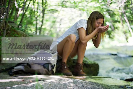 Female hiker drinking water from stream